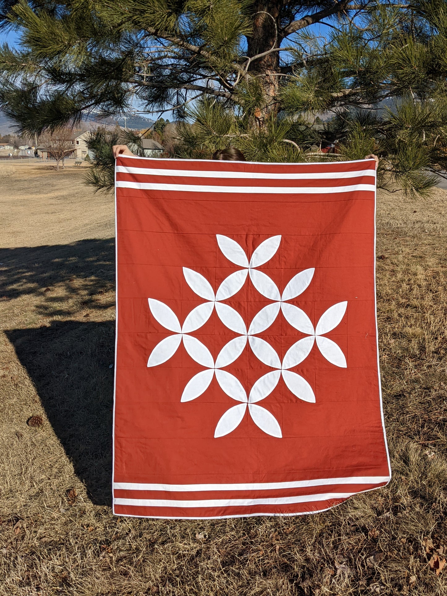 Orange and white modern orange peel quilt in front of tree.