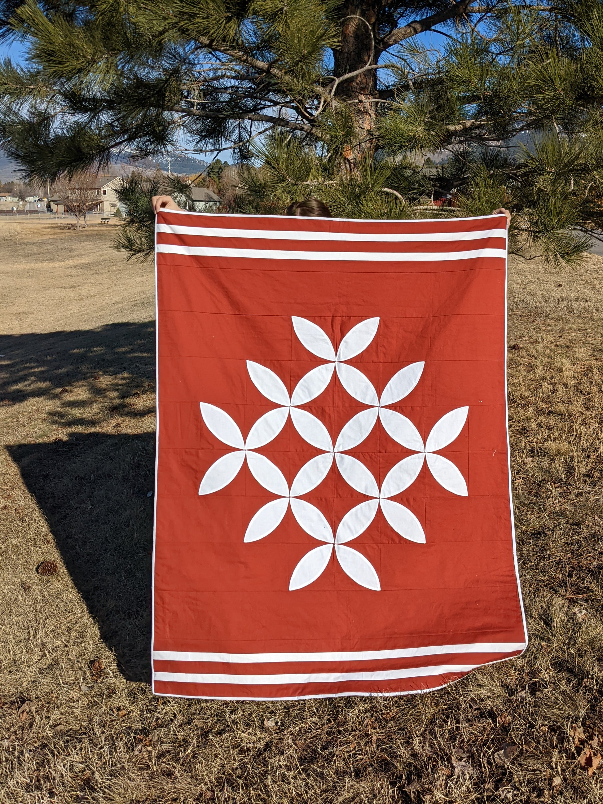Orange and white modern orange peel quilt in front of tree.