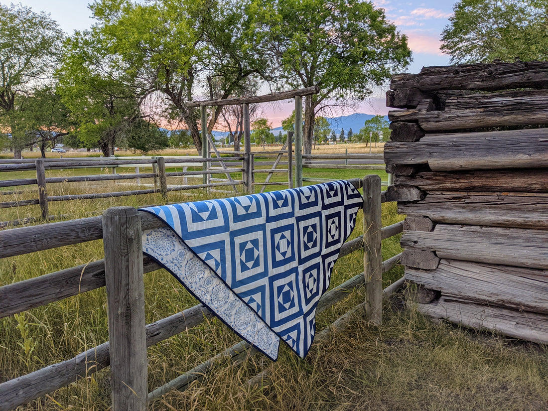 Modern quilt folded in half over a fence at sunset.