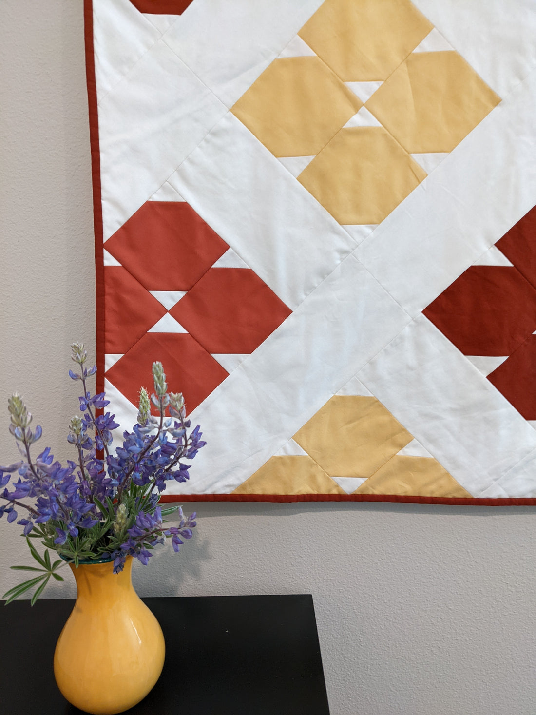 Yellow, pink orange and white quilt with purple flowers in yellow vase.