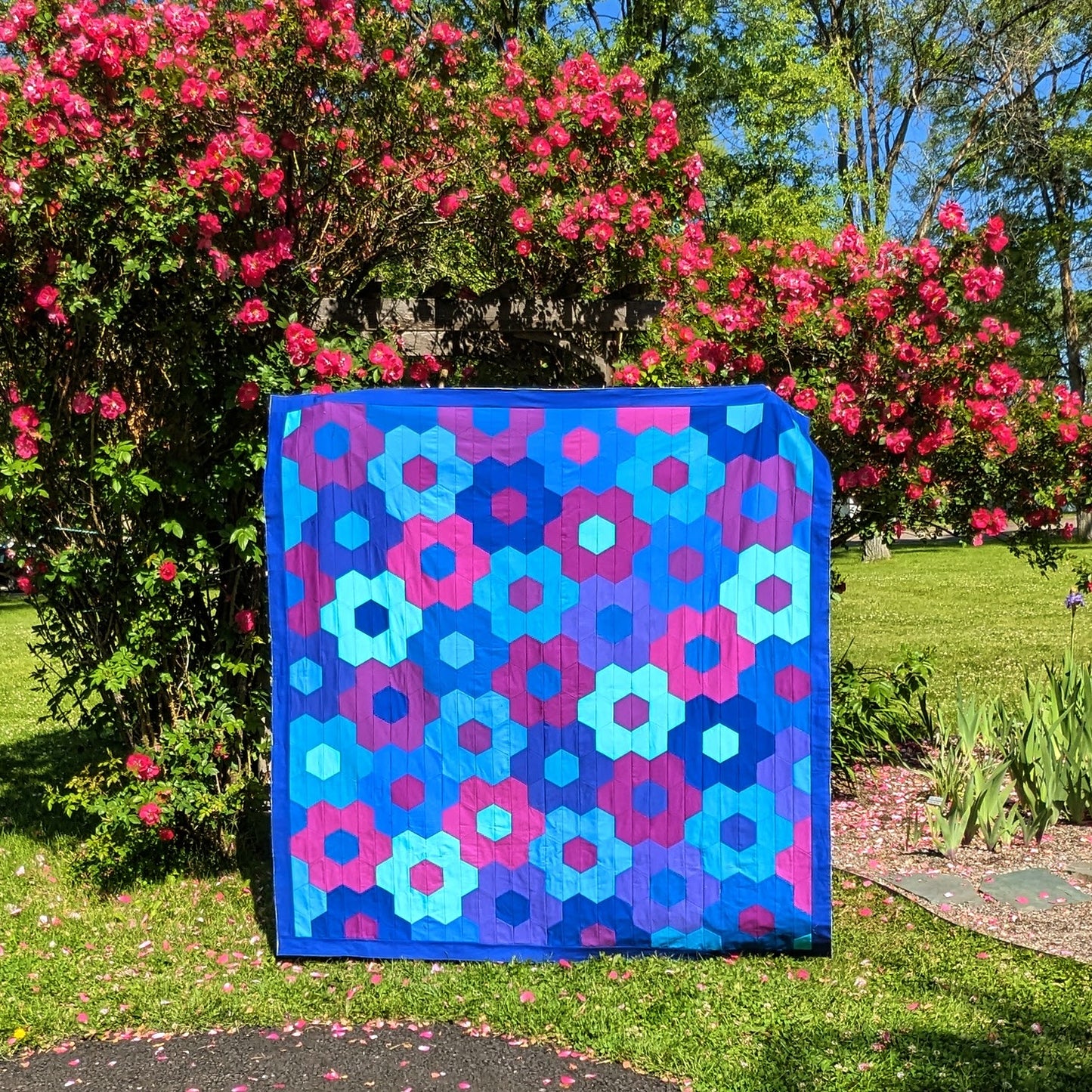 blue, purple and pink hexagon flower quilt in front of roses