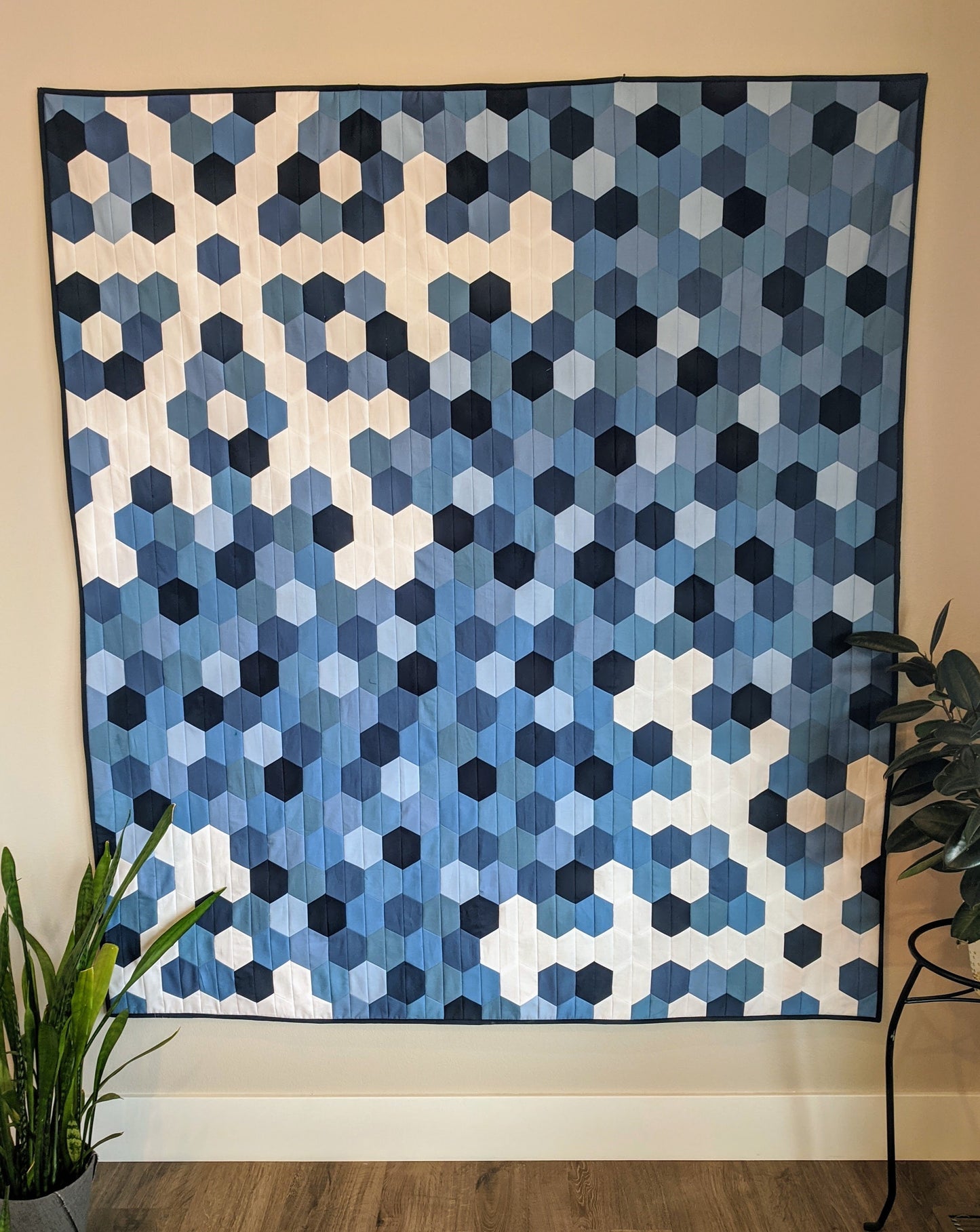 Scrappy blue and white snowflake and hexagon quilt on wall.