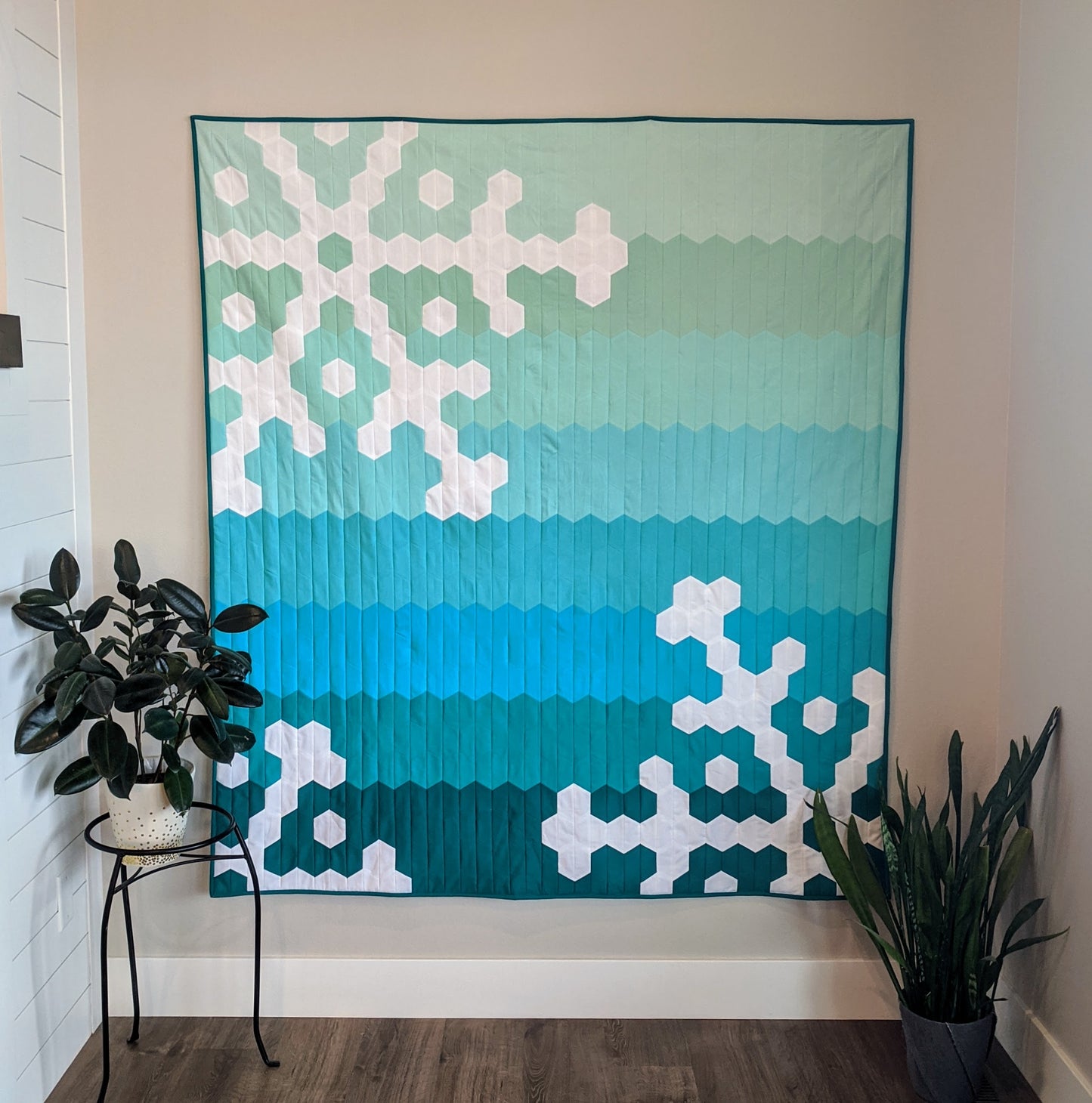 Ombre green and white snowflake and hexagon quilt on wall.