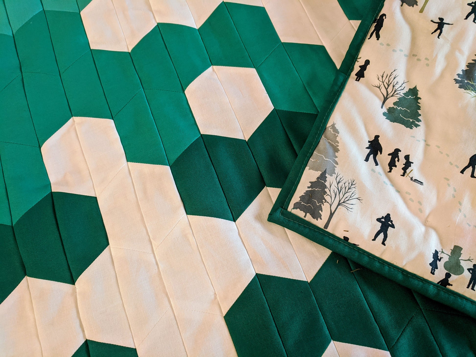 Green and white snowflake quilt with kids sledding on backing.