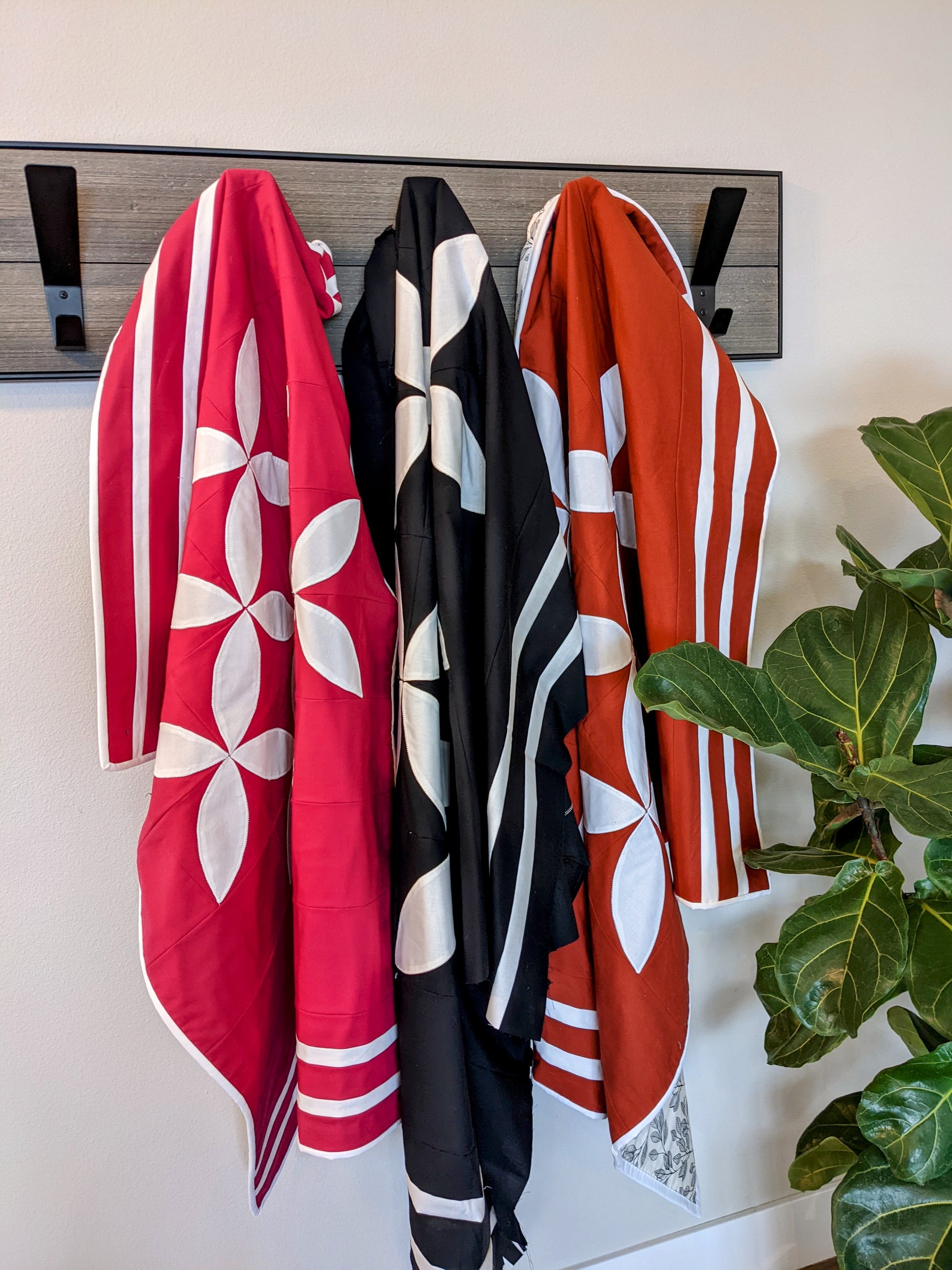Three modern quilts on coat rack with plant.